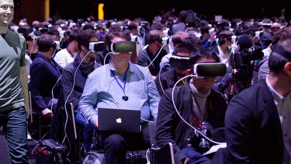 A photo of Mark Zuckerberg walking in front of a bunch of folks sitting wearing VR headsets
